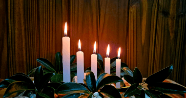 Cinco velas acessas em meio a plantas e em um cenário feito de madeira.